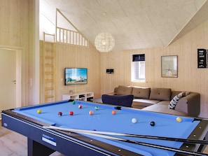 Ein Billardtisch mit Kugeln, eine Couch, ein Fernseher und eine Kristallleuchter in einem Raum mit Holzwänden.