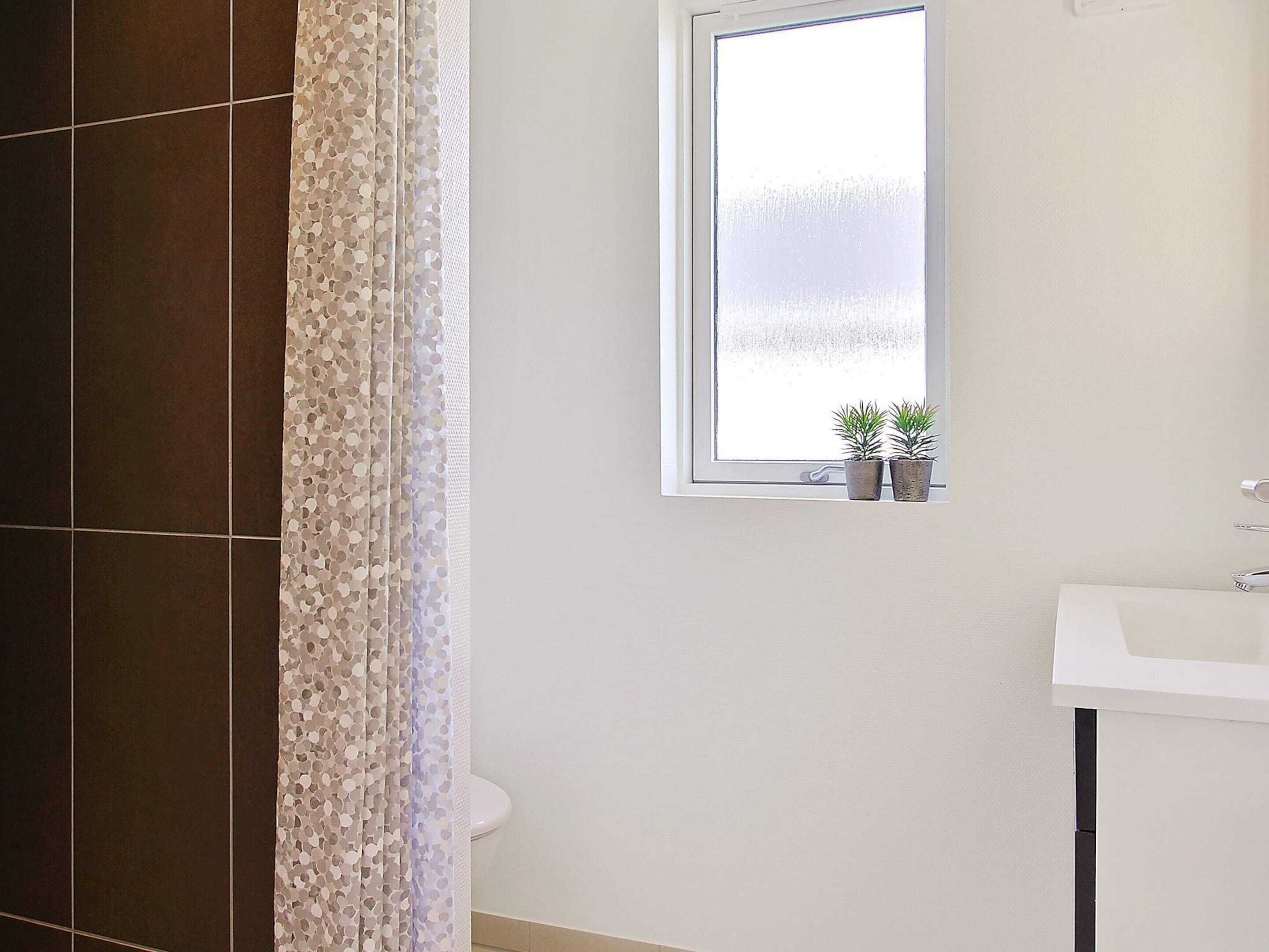 A bathroom with a window, a sink, and two potted plants.