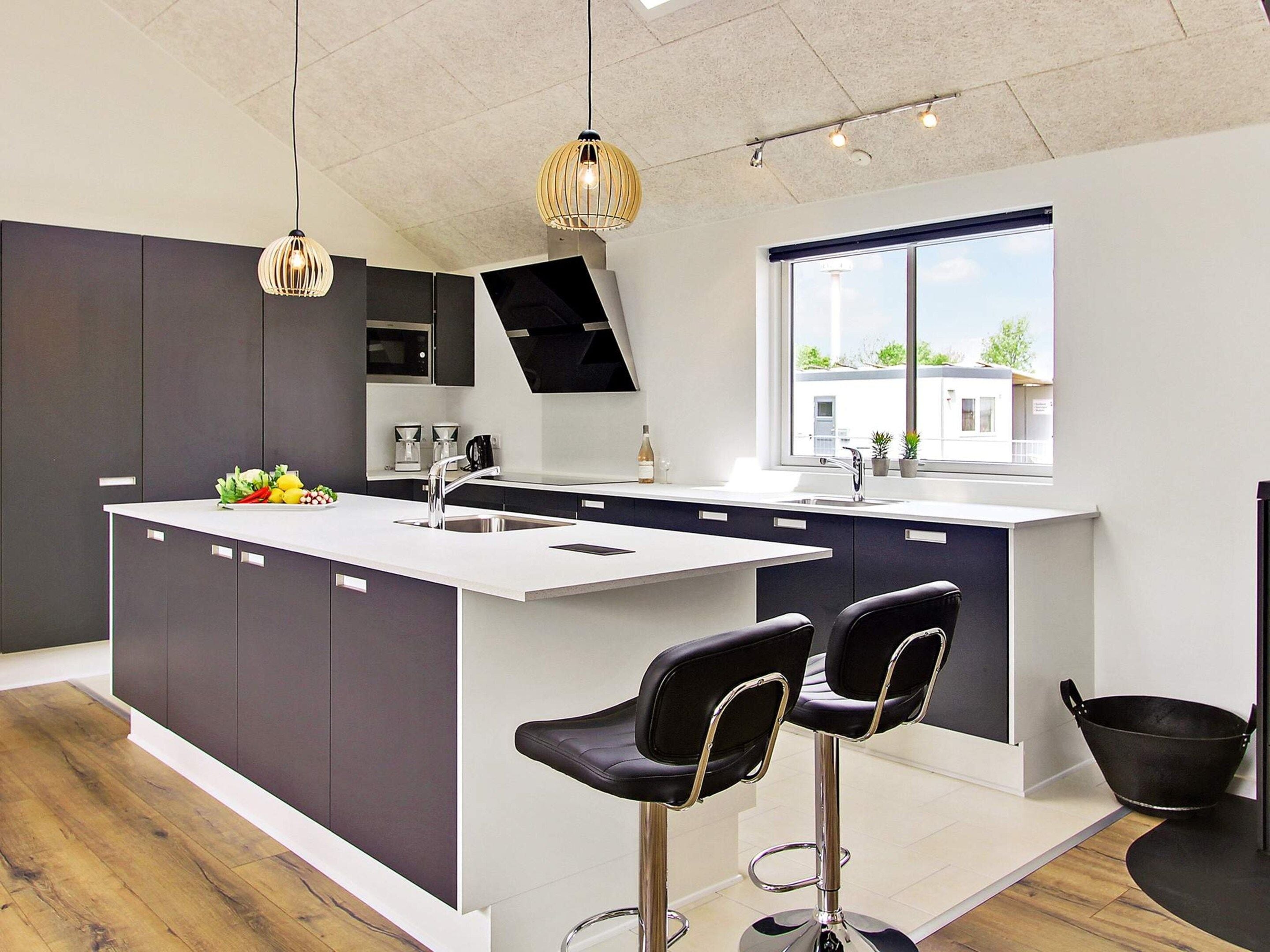A modern kitchen with a central island, bar stools, a large window, and pendant lighting.