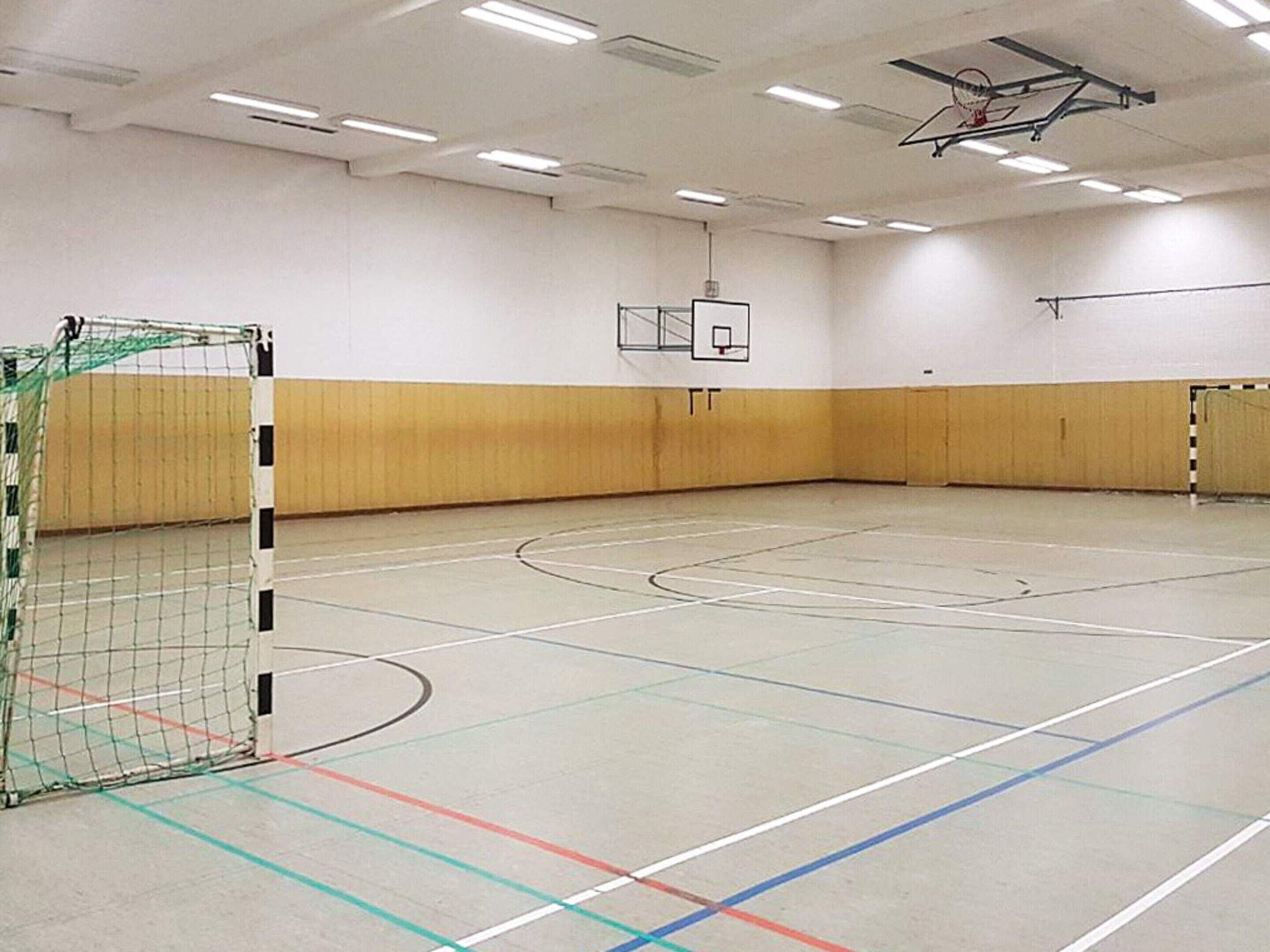 En indendørs basketballbane med kurv og en trævæg.