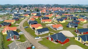 Un quartier résidentiel où les maisons, aux façades rouge et jaune, sont disposées selon un plan en forme de grille, avec des allées bien visibles et quelques voitures garées.