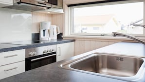 Eine moderne Küche mit weißen Schränken, einer Edelstahlspüle, einer Mikrowelle, einer Kaffeemaschine und einem Fenster mit Blick auf Gebäude.