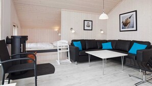 Ein gemütliches Zimmer mit Holzbalkendecke, einem schwarzen Ledersofa mit blauen Kissen, einem weißen Tisch und einem weißen Stuhl.