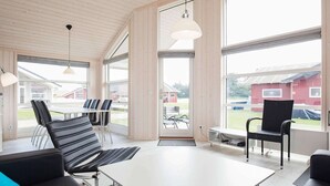 Ein modernes Interieur mit einem weißen Tisch, schwarzen Ledersesseln, großen Fenstern und einer Holzbalkendecke.