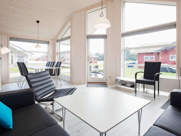 A modern interior with a white table and black leather chairs, large windows, and a wooden ceiling. - Holiday Home in Großenbrode (Grossenbrode)