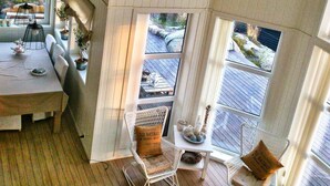 A cozy room with a dining table set for two, a comfortable seating area with cushions, and a view of a wooden deck outside.