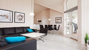 A modern interior with a black leather sofa, a white table, and black chairs. There are framed pictures on the wall and a large window with a view. - Holiday Home in Grossenbrode (Grossenbrode)