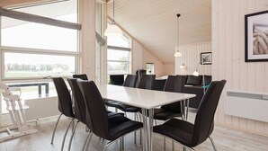 Moderni ruokailutila, jossa on suuri pöytä ja tuolit, suuret ikkunat ja puinen katto.