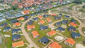 An aerial view of a residential area with houses featuring red roofs and grey exteriors, arranged in a grid pattern with visible driveways and pathways. - Holiday Home in Großenbrode (Grossenbrode)