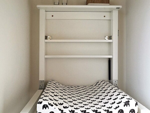 A small, narrow room with a white bed and a headboard with shelves.
