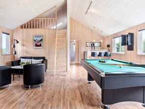A pool table with a green felt surface, a black sofa with cushions, a wooden ladder, and a poster on the wall.