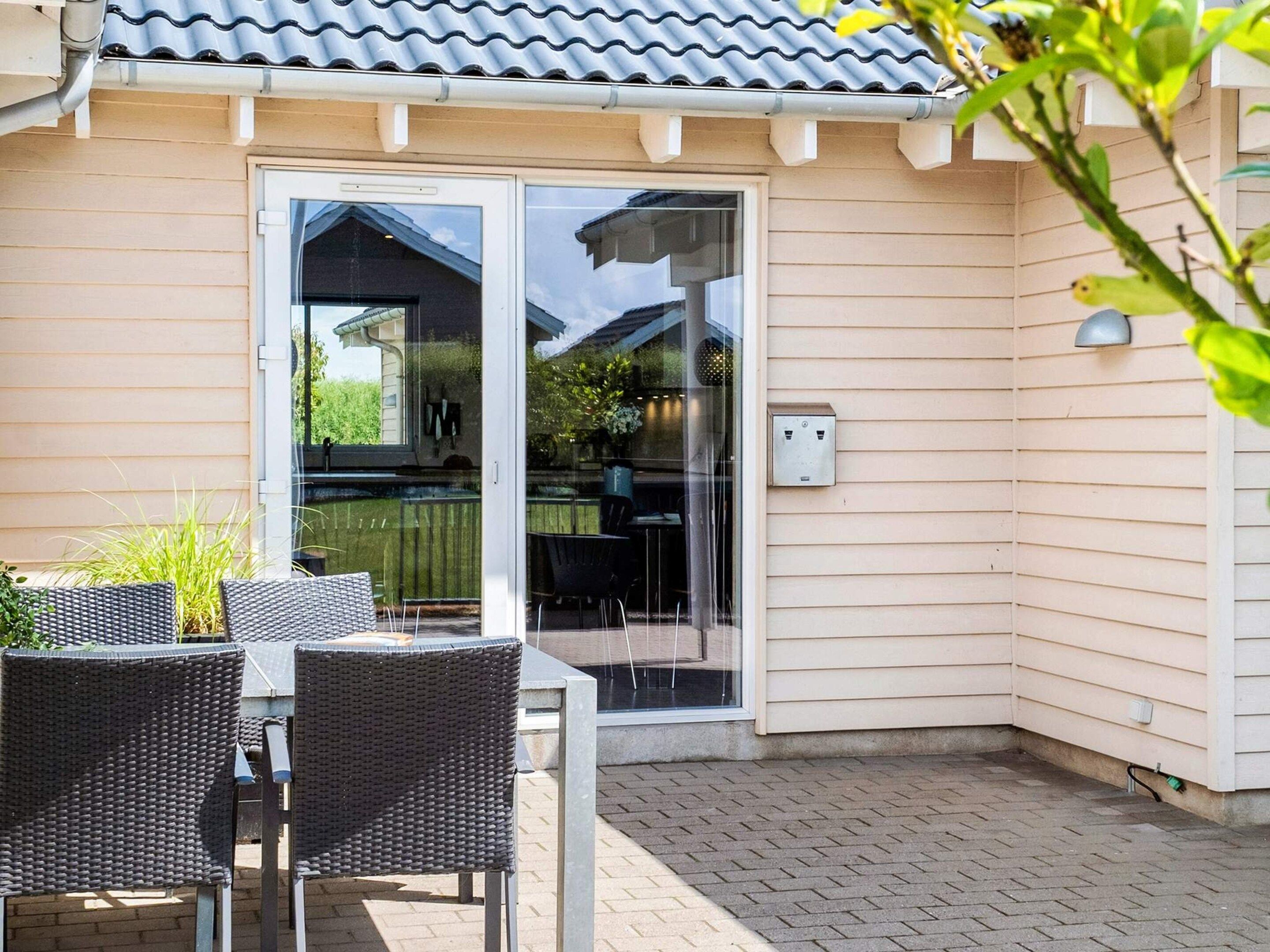 A patio with a table and chairs, a sliding glass door leading to a covered outdoor area, and a utility box on the wall.