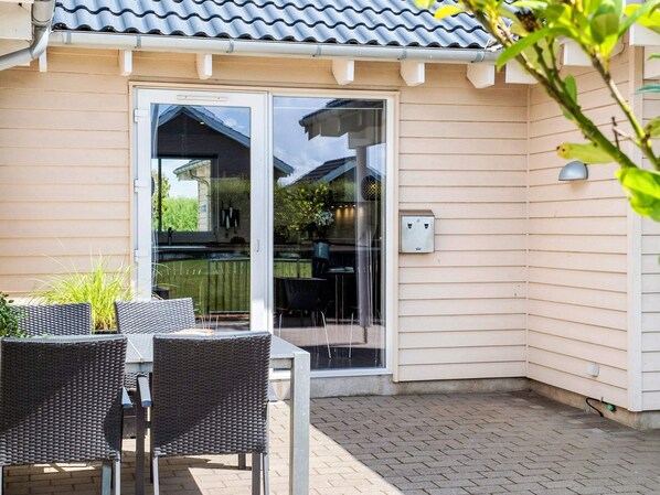 A patio with a table and chairs, a sliding glass door leading to a covered outdoor area, and a utility box on the wall.