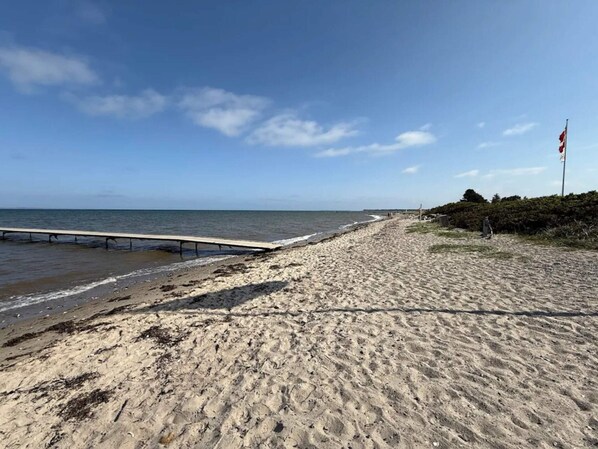 A beach with a wooden pier extending into the water, a sandy shore, and a flagpole with a flag. - 5 Star Holiday Home in Bogense (Bogense)