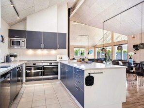 A modern kitchen with built-in appliances, a large island, and a dining area with wooden flooring and black chairs.