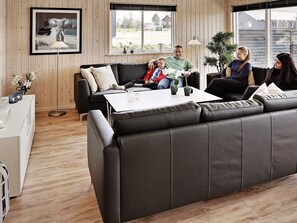 A modern living room with a black leather sofa, a white coffee table, and a wooden floor. There is a framed picture on the wall and a window with a view of the outside.