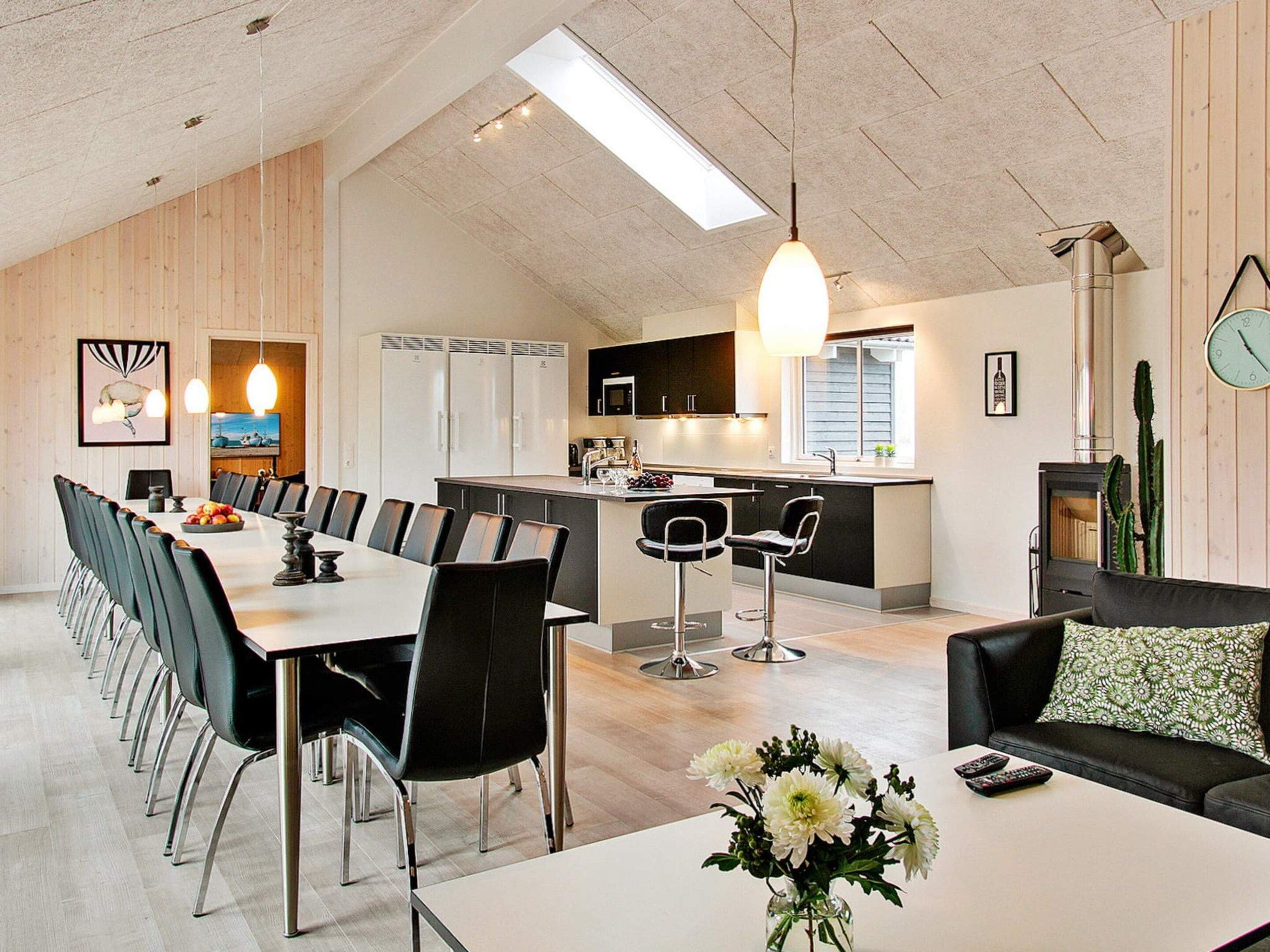 A modern kitchen with a central island, a dining area with a long table and chairs, and a living area with a sofa and a coffee table.