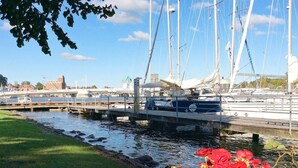 A marina with several sailboats docked, a grassy area with red flowers, and a bridge in the background. - Holiday Home in Kappeln (Kappeln)