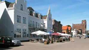 A square with white buildings, outdoor cafes, and a clock tower. - Holiday Home in Kappeln (Kappeln)