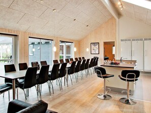 A modern dining area with long tables and chairs, a bar area, and a kitchen with vintage refrigerators.