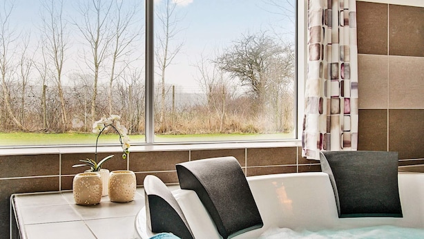 A modern bathroom with a large bathtub, a window with a view of trees, and a towel rack with towels. - Holiday Home in Kappeln (Kappeln)