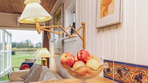 A cozy room with a wooden table, a bowl of fruit, a lamp, and a view of the outdoors. - Deluxe Holiday Home in Løkken near Sea (Lokken)