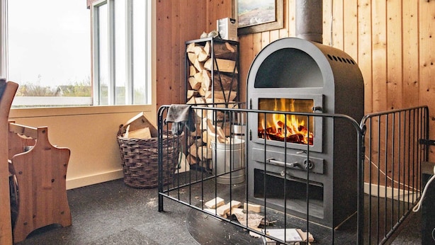 Ein gemütliches Zimmer mit Kaminofen, Fenster und Holzstuhl.