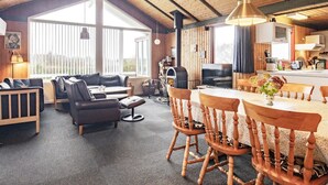 Ein gemütliches Wohnzimmer mit einer Couch, Sesseln und einem Esstisch. Ein Kamin und ein Fernseher sind ebenfalls vorhanden.