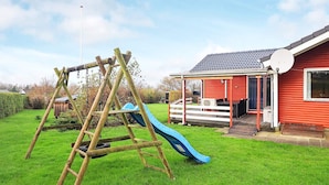 Eine Holzschaukel und eine blaue Rutsche in einem grünen Garten, im Hintergrund ein rotes Haus.