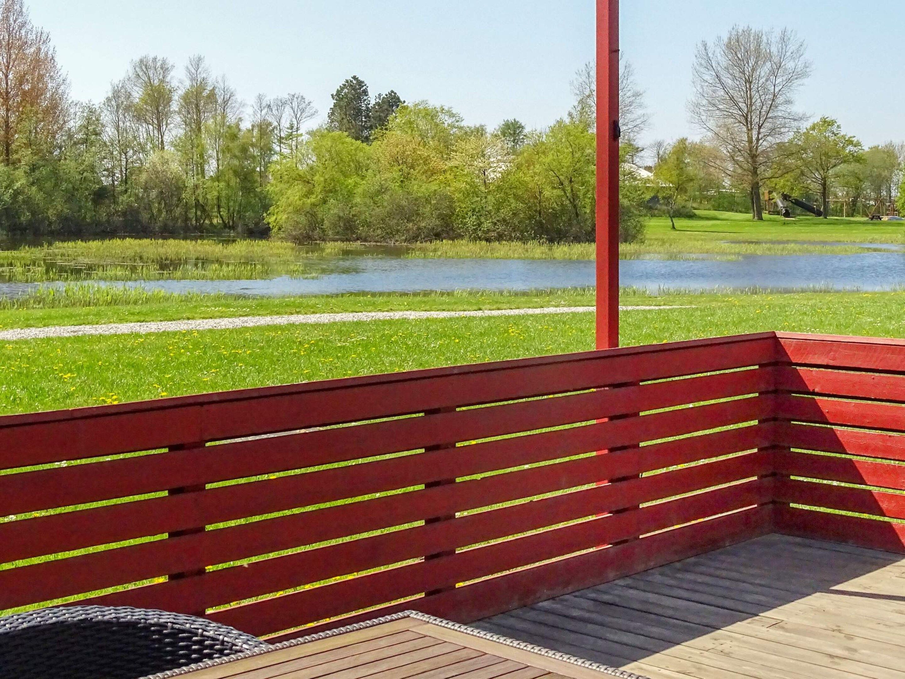 A wooden deck with a red bench overlooking a pond and trees.