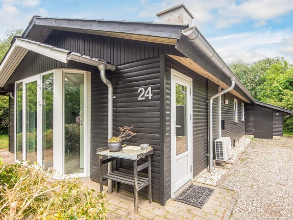Une maison en bois noire, portant le numéro 24, avec une petite table sur laquelle se trouve une plante, et une porte.