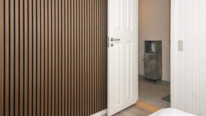 Een kamer met een wand van houten latten, een witte deur en een kleine keuken in de achtergrond.