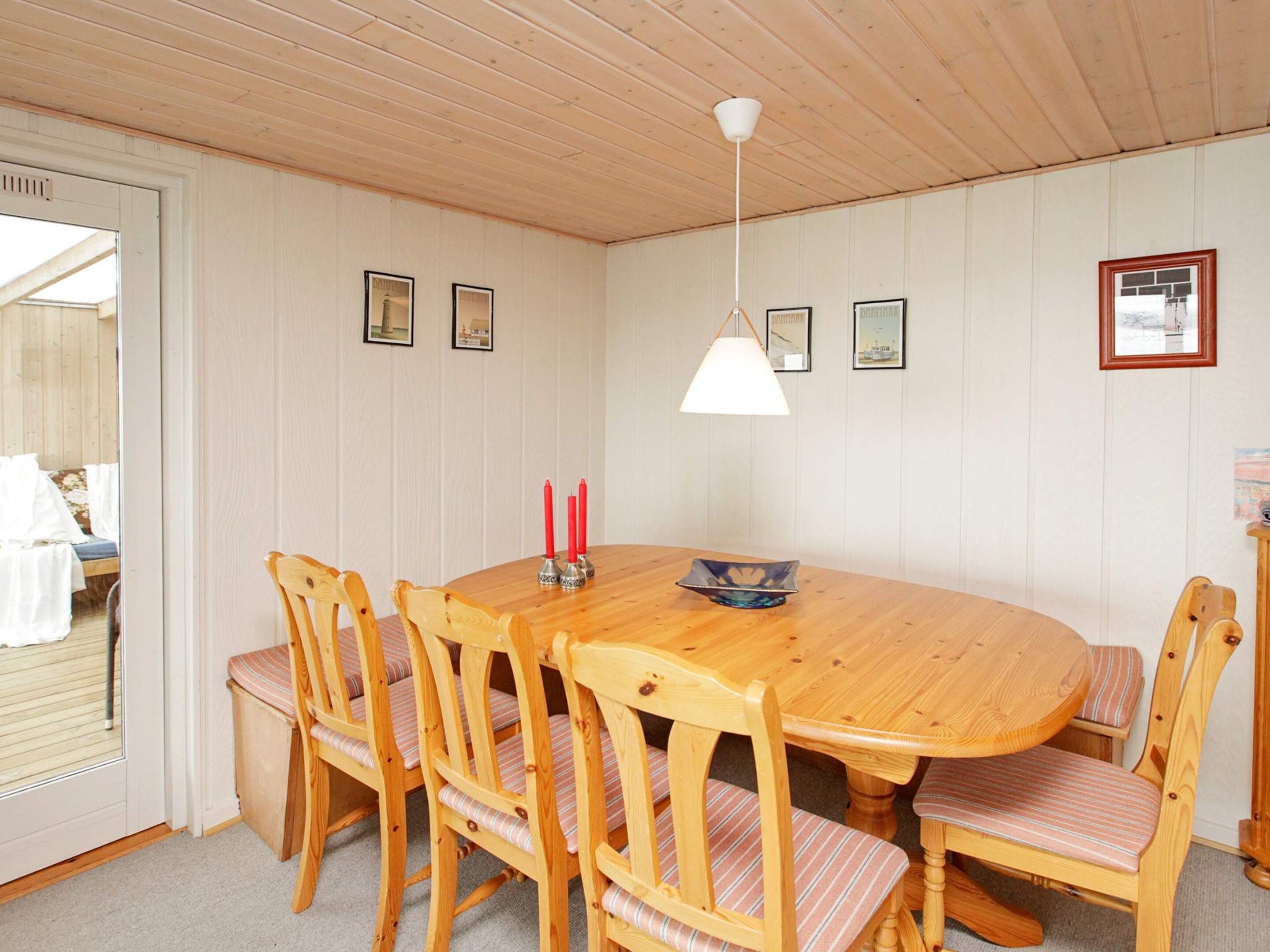 A dining area with a wooden table and chairs, a hanging light fixture, and framed pictures on the wall.