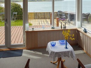 A room with a view of the sea, a table with a vase of flowers, and a chair.