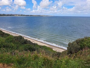 A coastal landscape with a beach, vegetation, and a clear sky.
