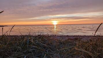 Uma praia com grama ao primeiro plano e um pôr do sol sobre a água.