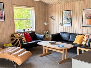 A cozy room with a black leather sofa, a wooden coffee table, and a window with a view of greenery. - 4 Star Holiday Home in Tarm (Tarm)