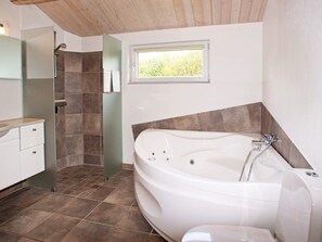 A bathroom with a large bathtub, a shower area, and a window providing natural light. - 4 Star Holiday Home in Tarm (Tarm)