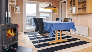 A cozy room with a wood-burning stove, a dining table with chairs, a black and white striped rug, and a wooden cabinet with glass doors. - 4 Star Holiday Home in Albaek (Aalbaek)