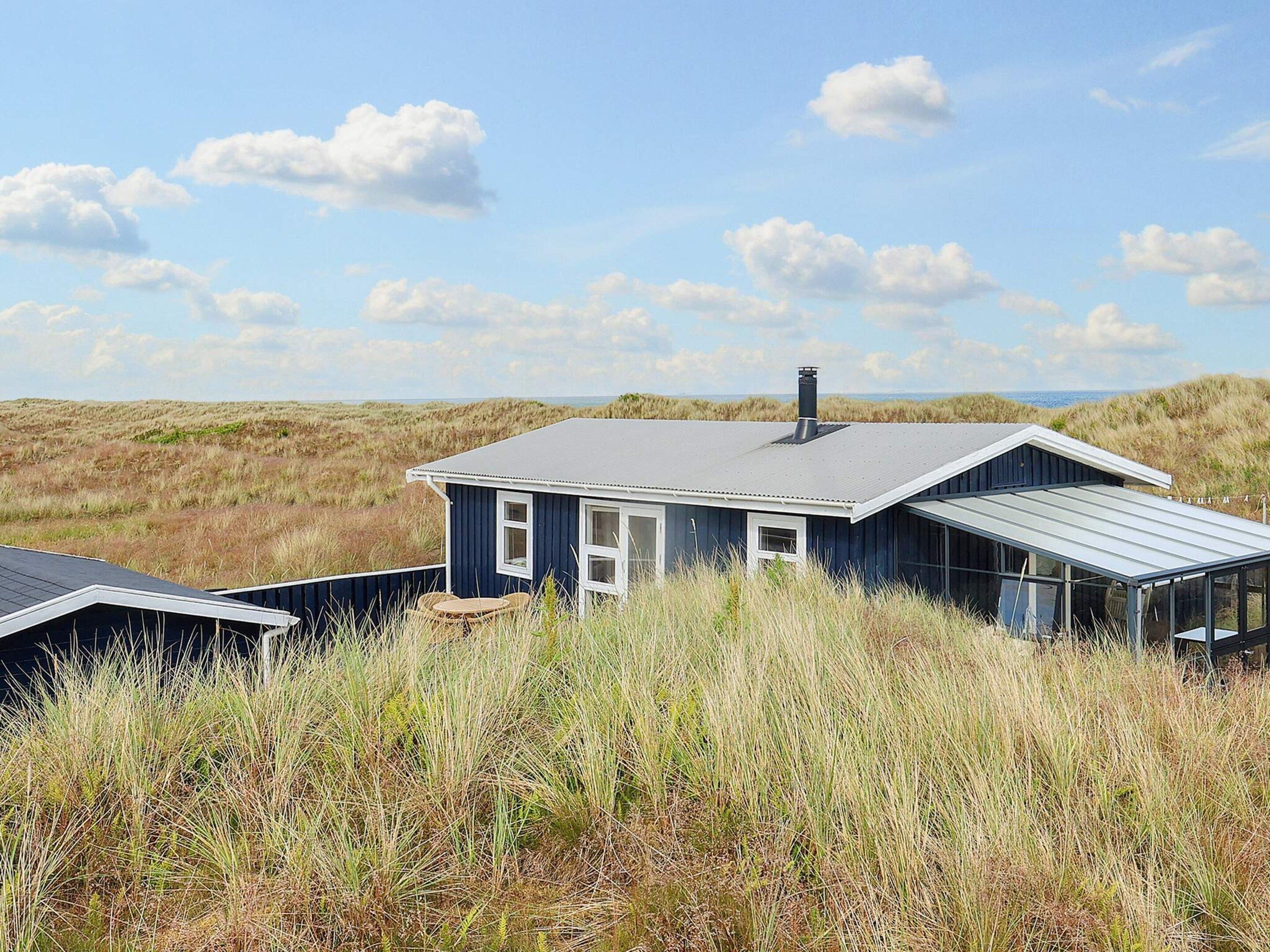 A coastal house with a dark blue exterior, a grey roof, and a glass conservatory.