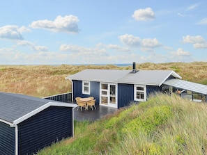 Une maison située sur la côte, dotée d’une terrasse, d’un coin repas et offrant une vue sur les dunes.
