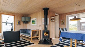 A cozy room with a wooden interior, a sofa, a dining table with chairs, a fireplace, and a TV mounted on the wall. - 4 Star Holiday Home in Albaek (Aalbaek)