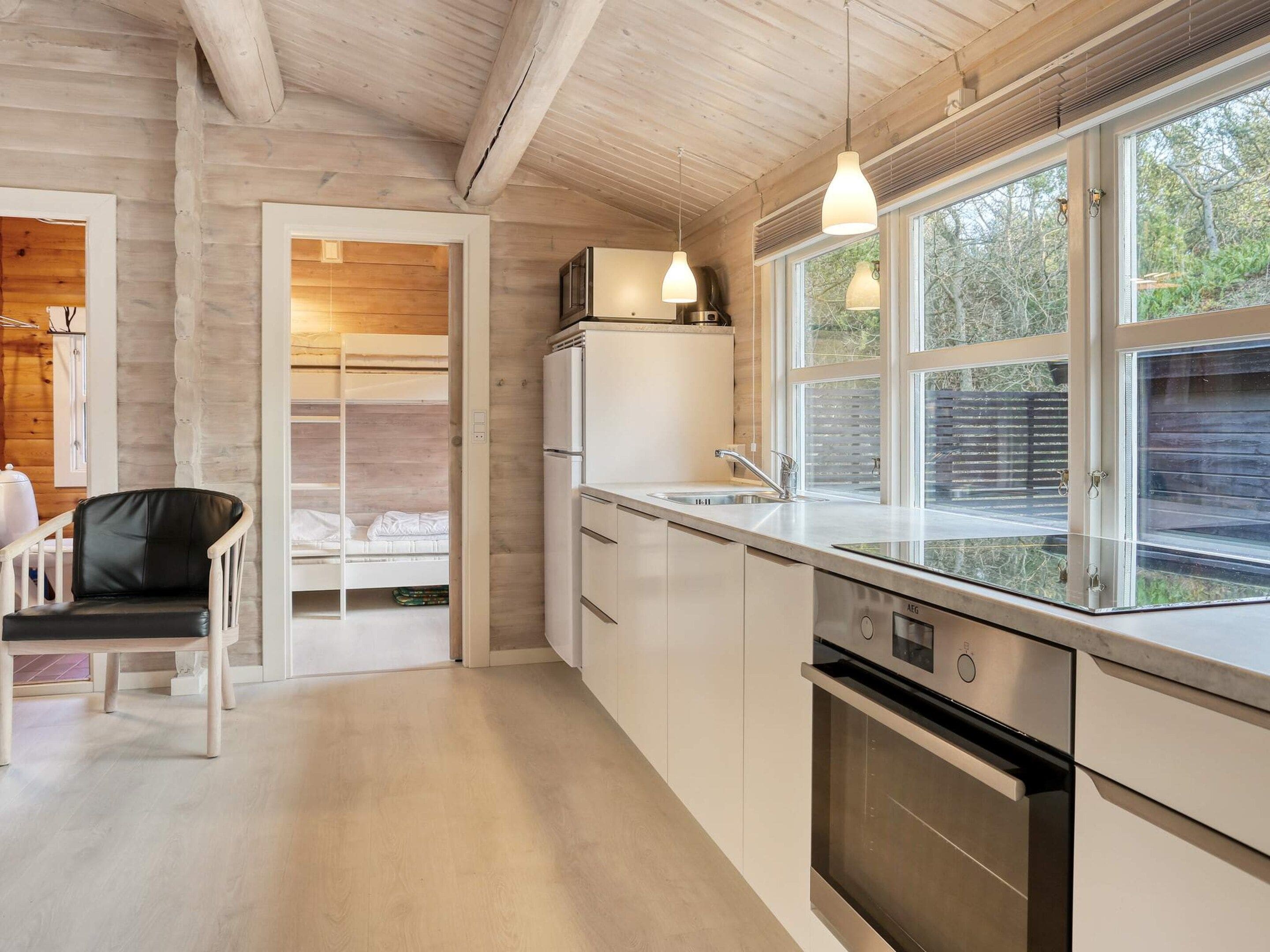 A modern kitchen with a built-in oven, a refrigerator, and a window with blinds.