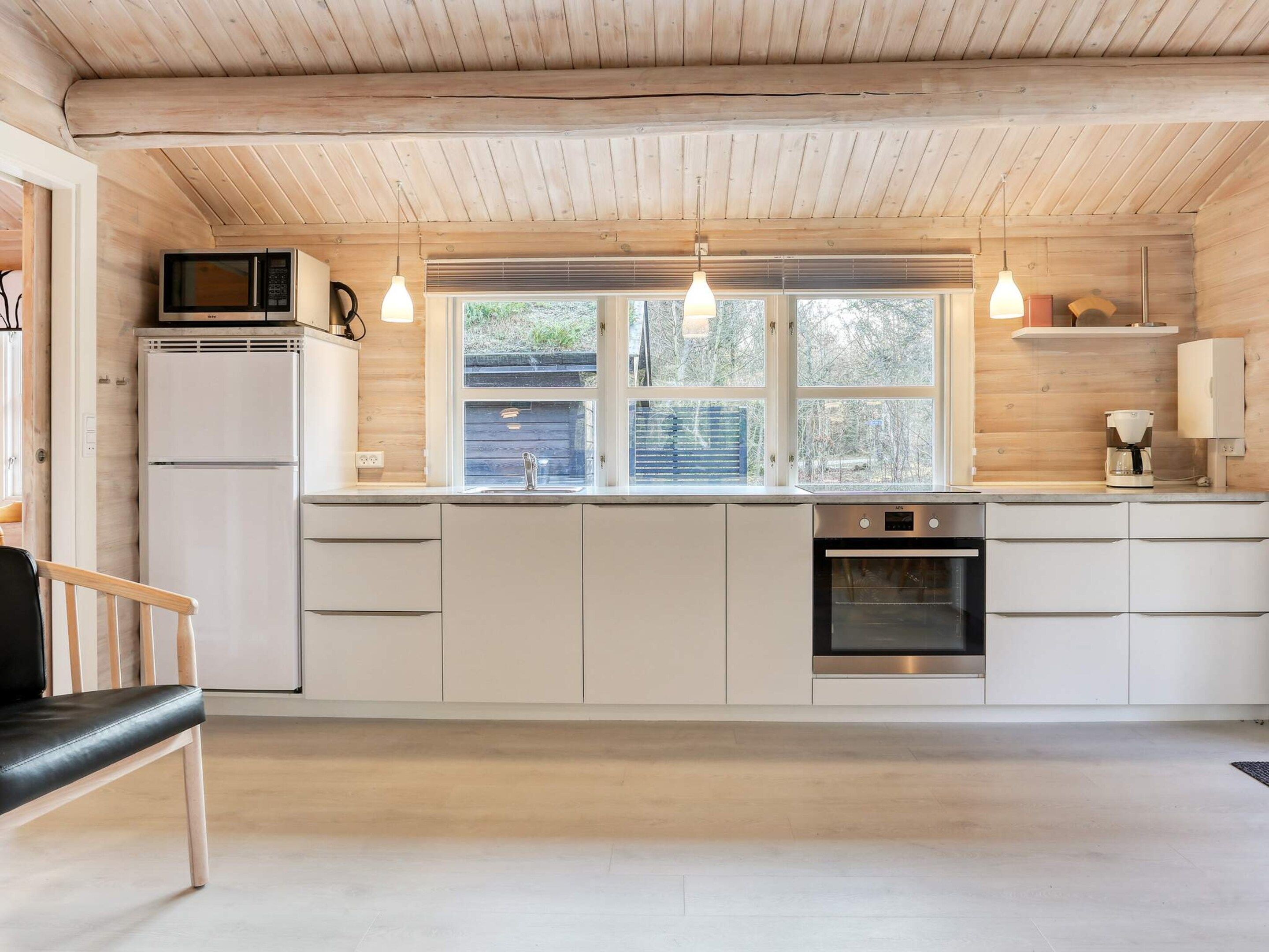 A modern kitchen with wooden ceiling beams, white cabinetry, a built-in microwave, and a coffee machine.