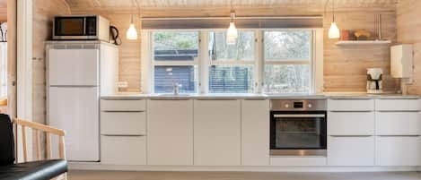 A modern kitchen with wooden ceiling beams, white cabinetry, a built-in microwave, and a coffee machine.