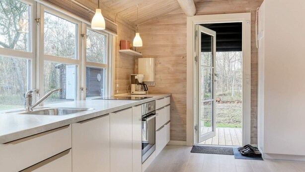 A modern kitchen with white cabinets, a stainless steel sink, and a coffee maker. There are large windows and a door leading outside.