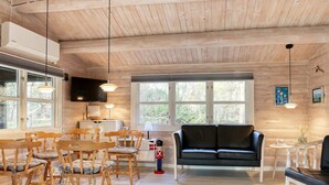 A cozy wooden interior with a black leather sofa, wooden chairs, and a dining table.