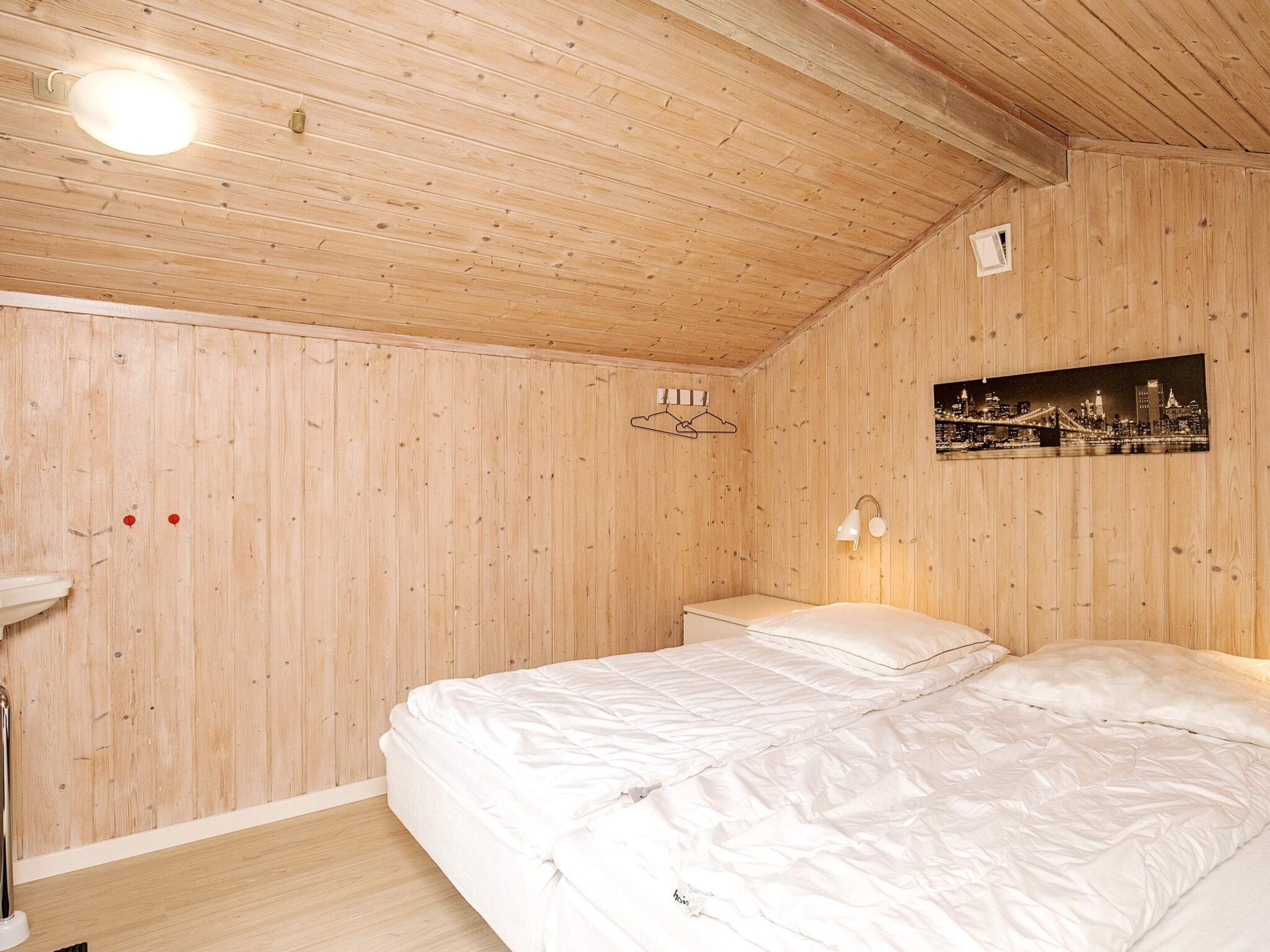 A wooden-paneled room with a bed, a nightstand, a wall-mounted light, and a framed picture.