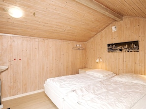 A wooden-paneled room with a bed, a nightstand, a wall-mounted light, and a framed picture.