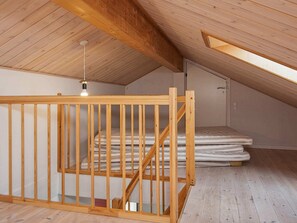 Un escalier en bois mÚne à une chambre située en mezzanine, avec un plafond en pente et un puits de lumiÚre.